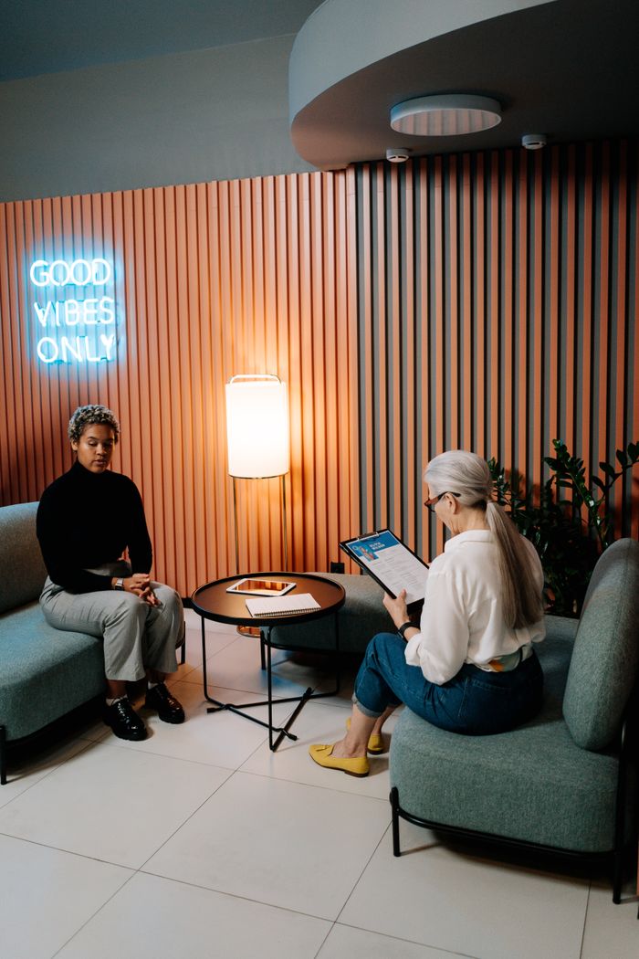Serviços Two professional women engaged in a business meeting in a modern office lounge.