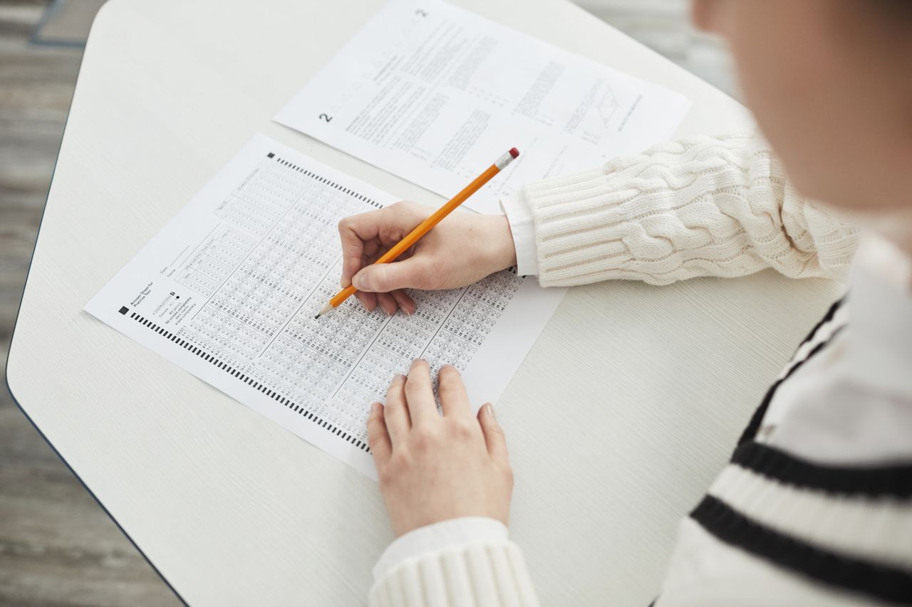 Home Close-up of a student filling out a multiple-choice exam in a quiet classroom setting.