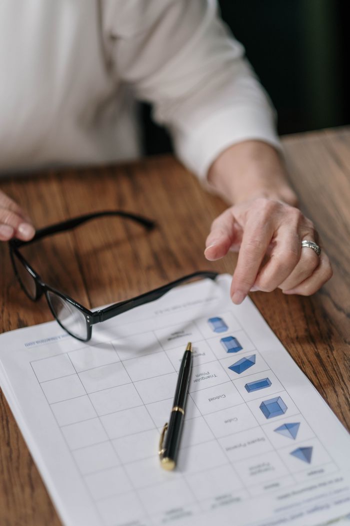 Home A person reviews paperwork with a pen and glasses on a wooden surface, emphasizing business analysis.