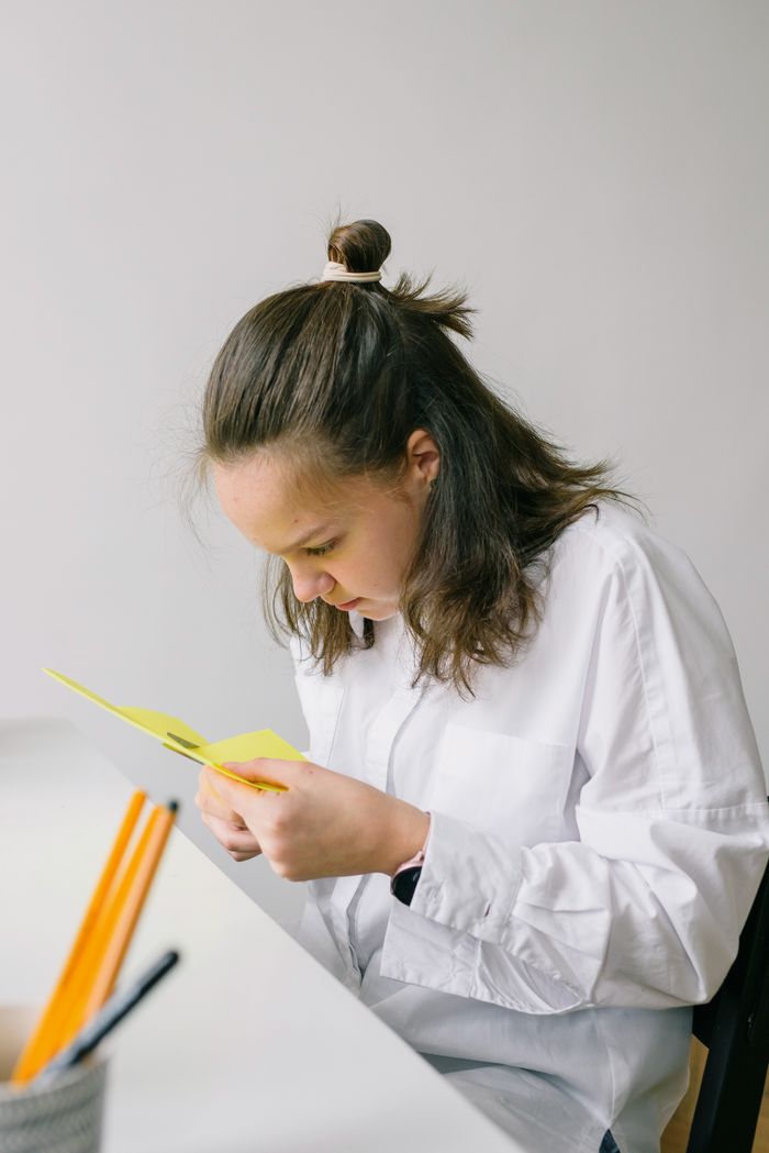 Serviços Young woman in white shirt intensely reading a yellow card indoors.