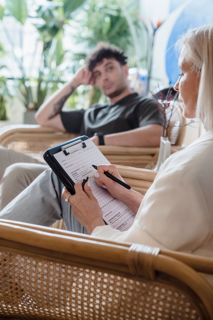 Home Therapist takes notes during a counseling session with a thoughtful client.