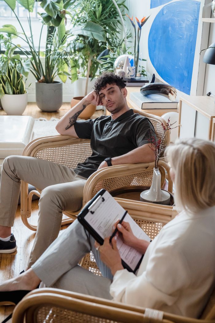 Serviços A man and a woman in a therapeutic counseling session in a plant-filled modern office space.